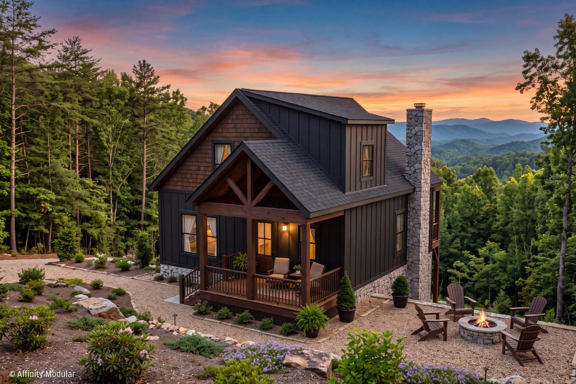 Modern modular home with porch and fire pit, surrounded by trees and mountains at sunset.