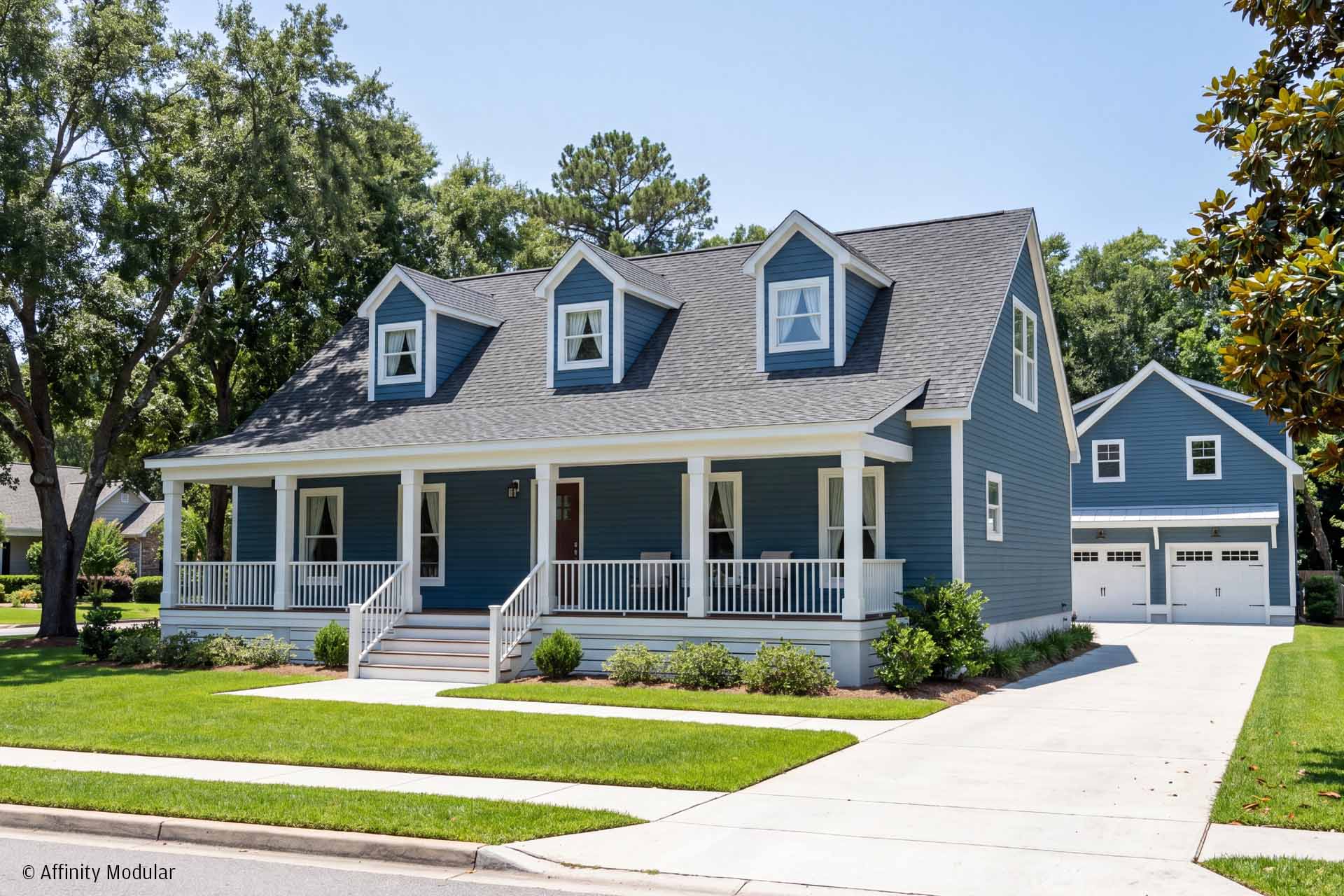 A blue two-story modular home with a front porch, dormer windows, and a detached garage, surrounded by green lawns.