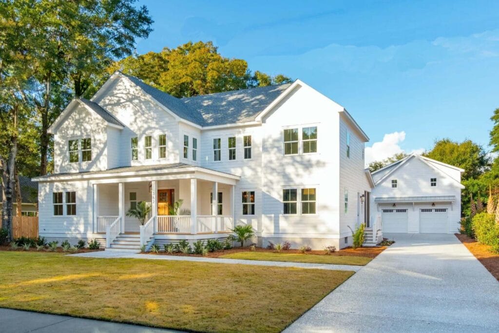 Modern two-story white modular home with a front porch, double garage, and well-kept lawn under a blue sky.