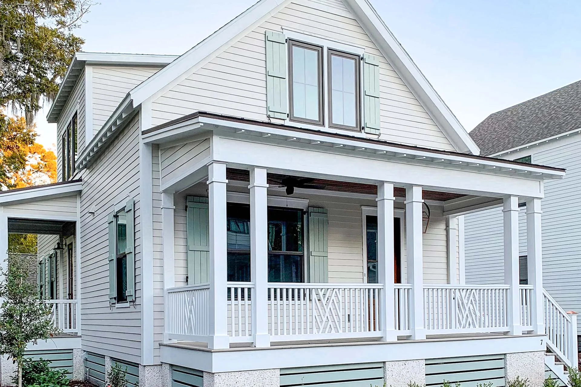 White modular home with green shutters, a covered front porch, and railing on a sunny day.