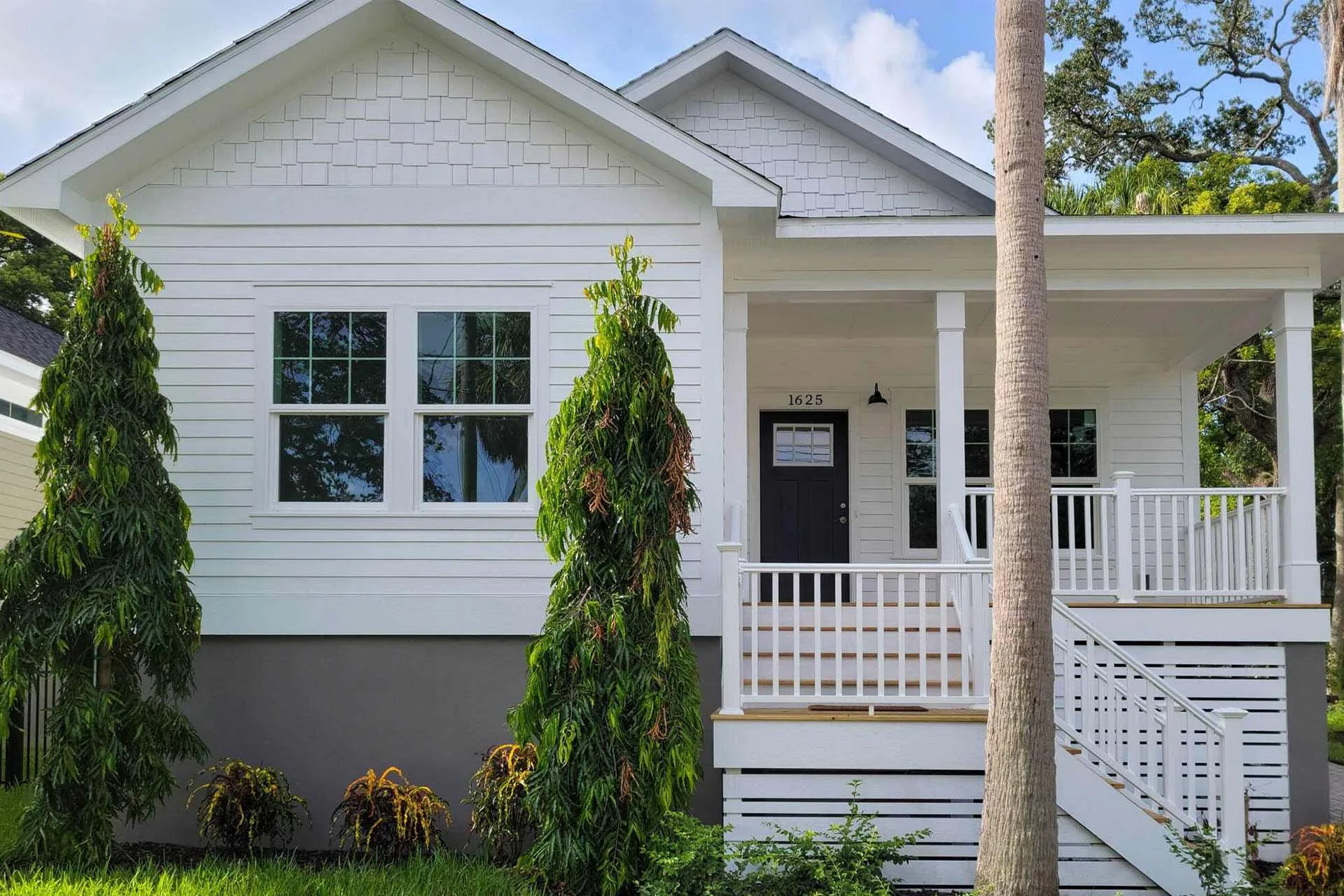 A white modern modular home featuring a front porch, steps, and two tall green bushes in the yard.