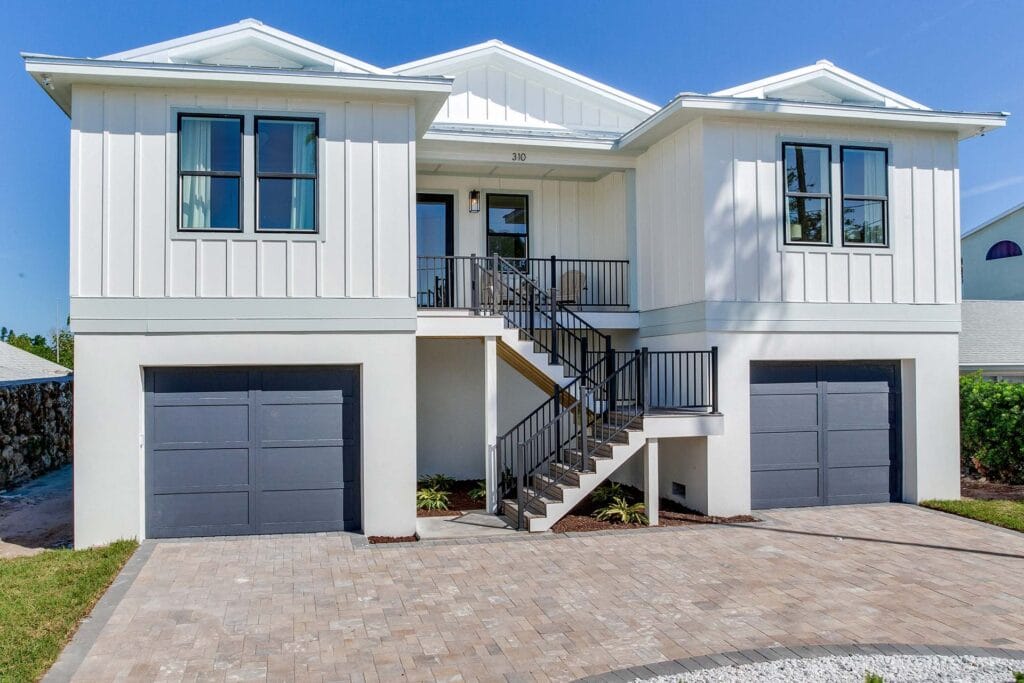 Modern white modular home with black garage doors, central steps, and a paved driveway under a clear blue sky.