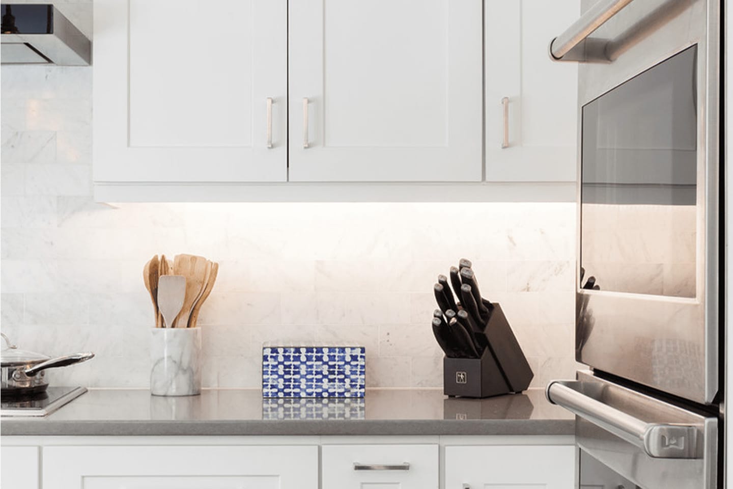 Modern kitchen with white cabinets, knife block, utensils in a jar, and a blue patterned tray on the counter.